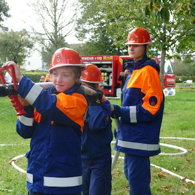 Drei Kinder der Jugendfeuerwehr Tropisdorf-Altenrath spritzen Wasser mit einem Schlauch.