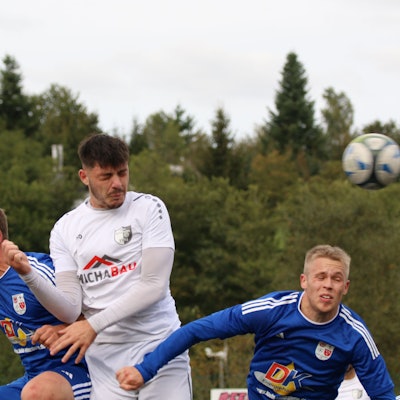 Drei Fußballer springen zum Kopfball hoch. Alle drei haben die Augen geschlossen.