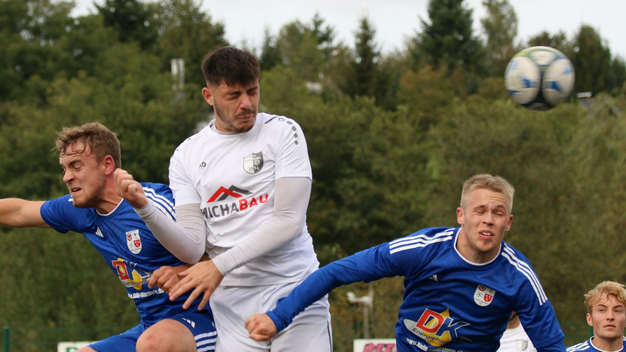 Drei Fußballer springen zum Kopfball hoch. Alle drei haben die Augen geschlossen.