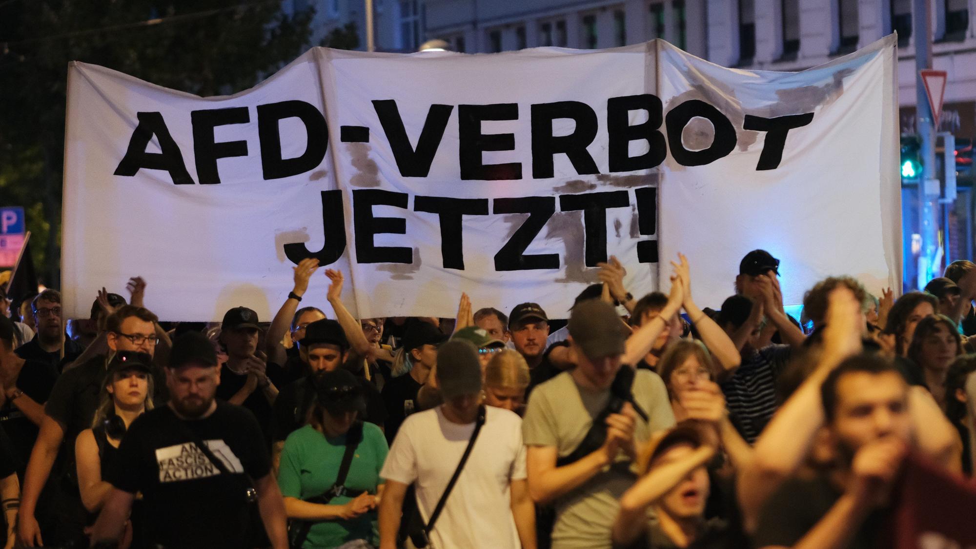 Teilnehmer einer linken Demonstration gehen mit Transparent mit der Aufschrift «AfD- Verbot jetzt!» eine Straße entlang.