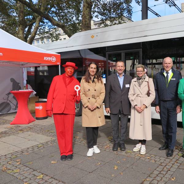 Anja Höhn (2.v.l.), Patric Stieler (3.v.l.) und Martin Lotz (2.v.r.) stehen zwischen zwei menschlichen Ampelmännchen vor einem Bus der KVB.
