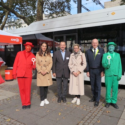 Anja Höhn (2.v.l.), Patric Stieler (3.v.l.) und Martin Lotz (2.v.r.) stehen zwischen zwei menschlichen Ampelmännchen vor einem Bus der KVB.