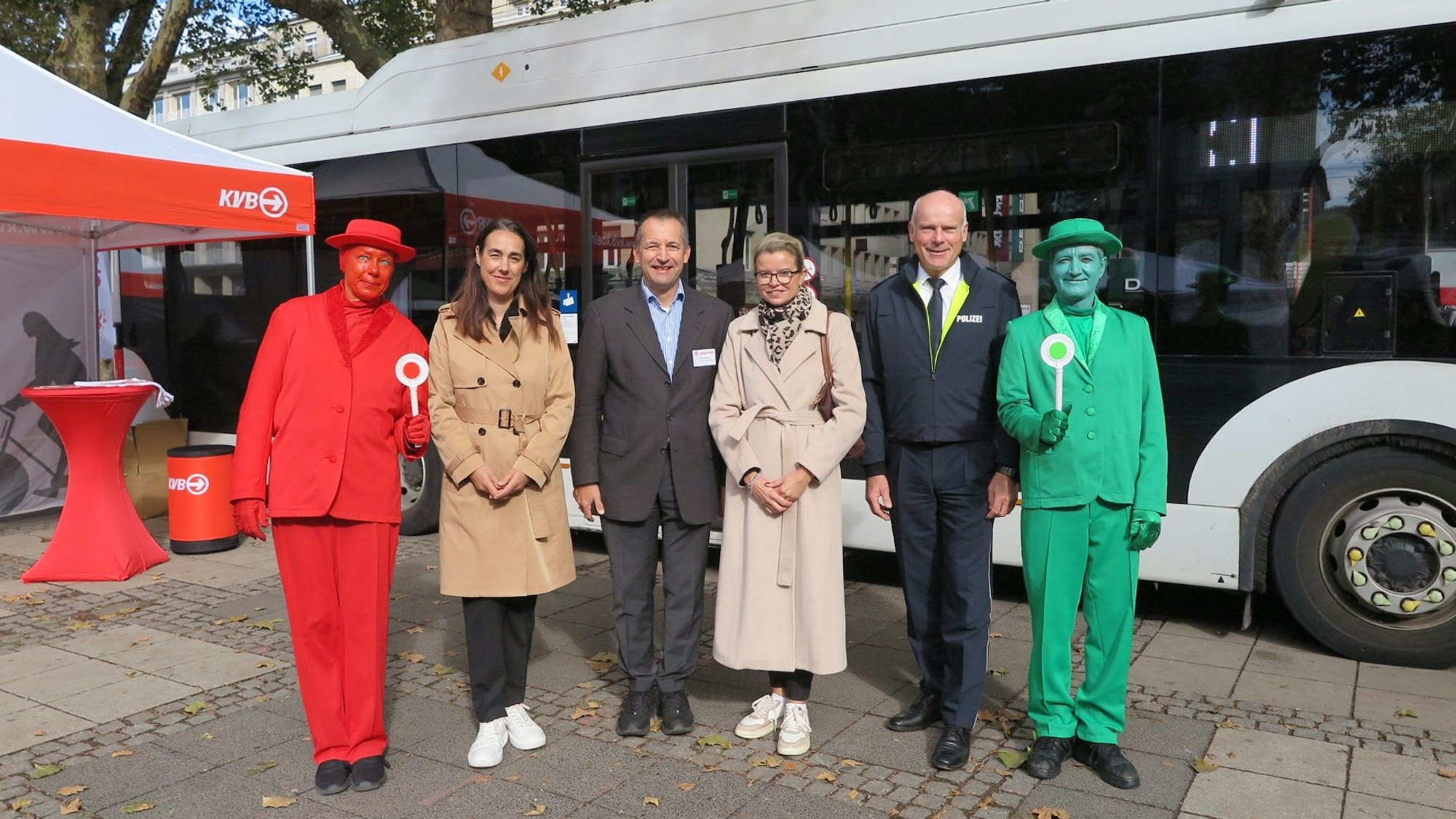 Anja Höhn (2.v.l.), Patric Stieler (3.v.l.) und Martin Lotz (2.v.r.) stehen zwischen zwei menschlichen Ampelmännchen vor einem Bus der KVB.