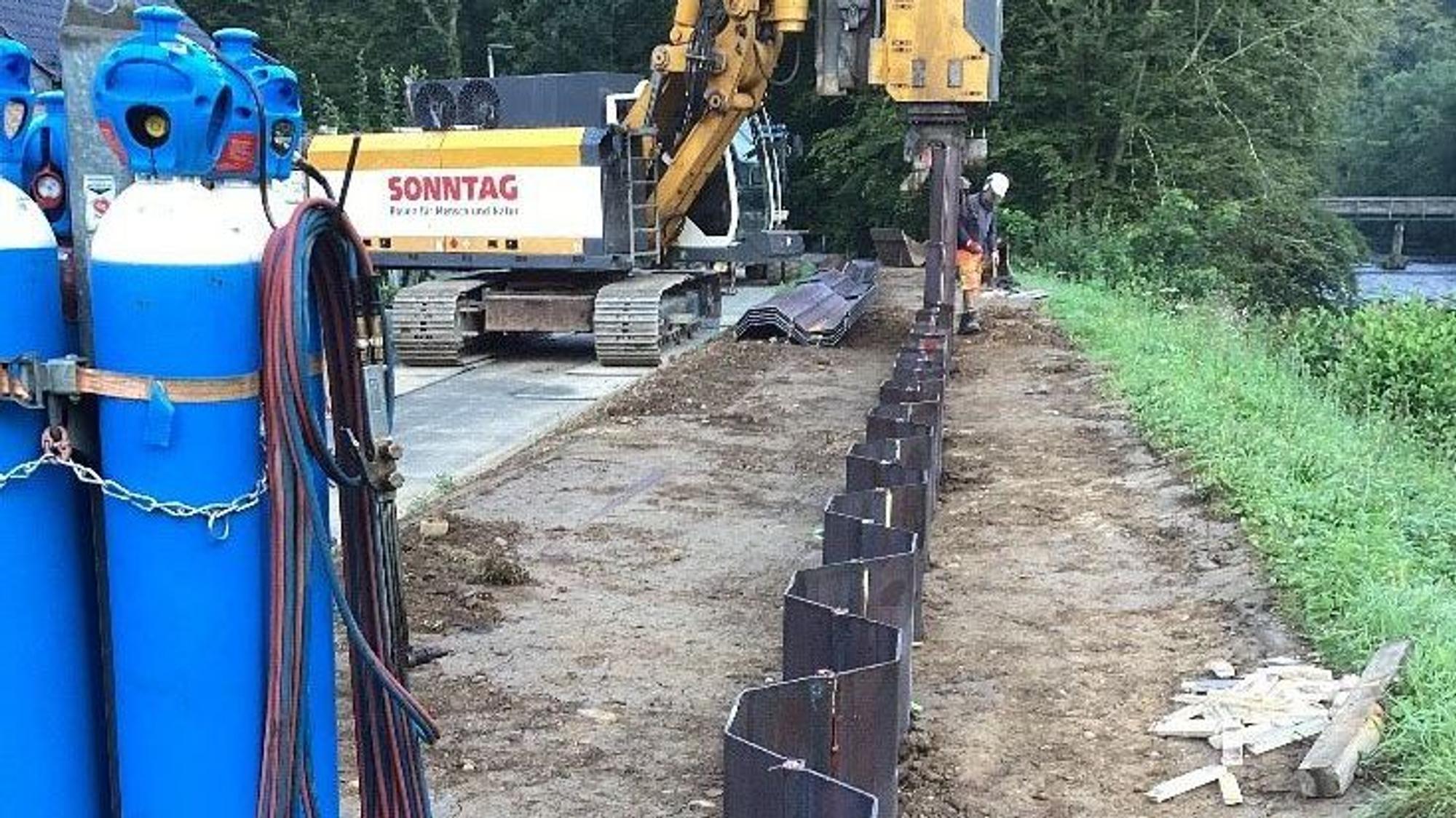 Ein Bagger und ein Bauarbeiter am Flussufer