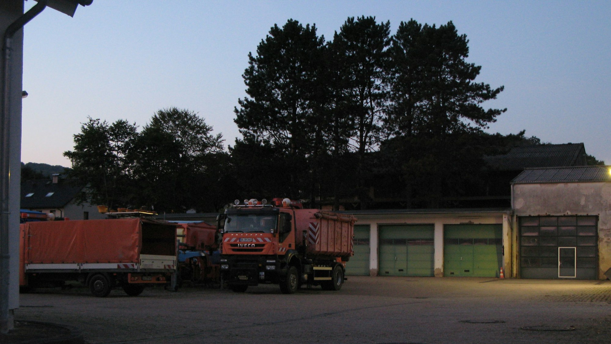 Blick auf einen asphaltierten Hof mit Hallen und orangefarbenen Lastwagen.