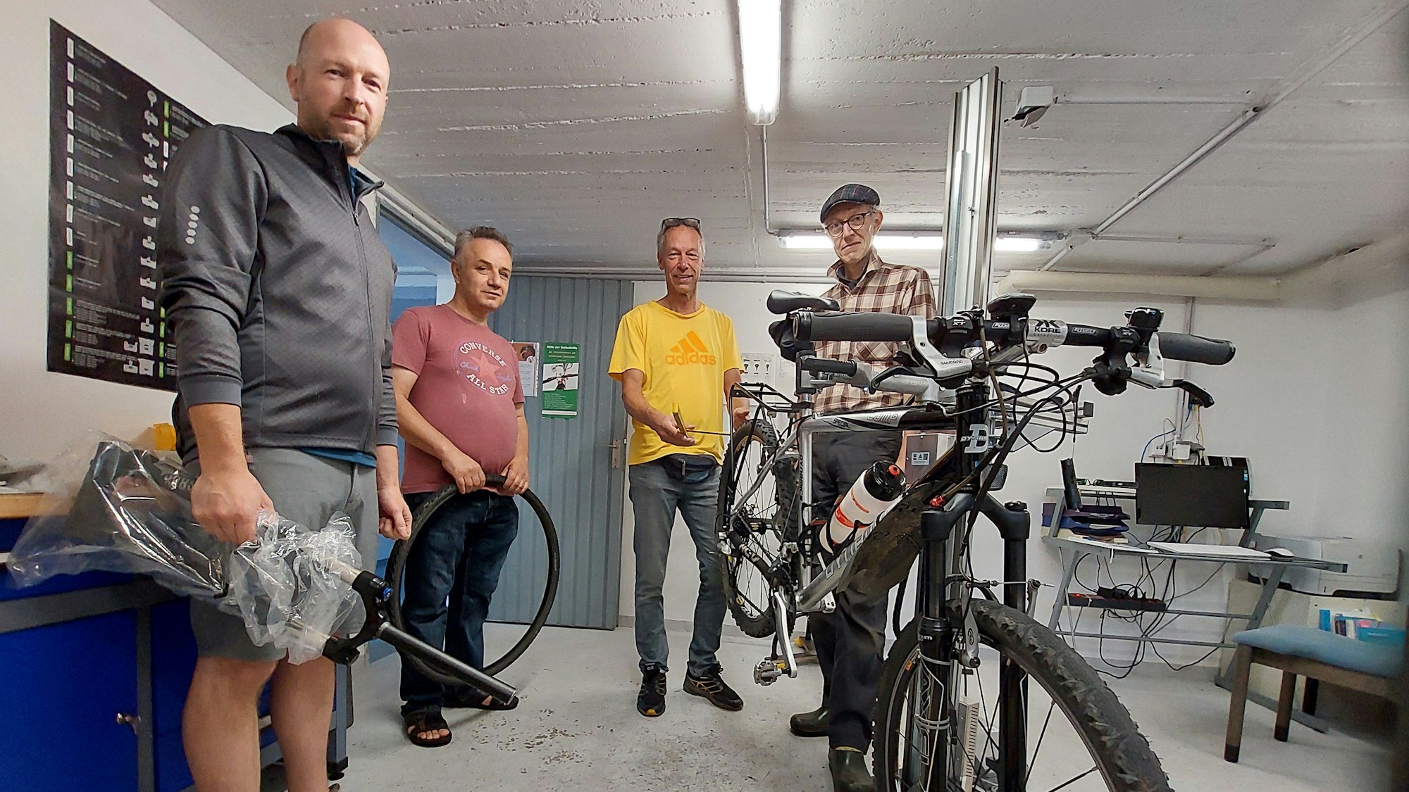 Vier Männer stehen in einem Raum, ein Fahrrad ist aufgebockt.