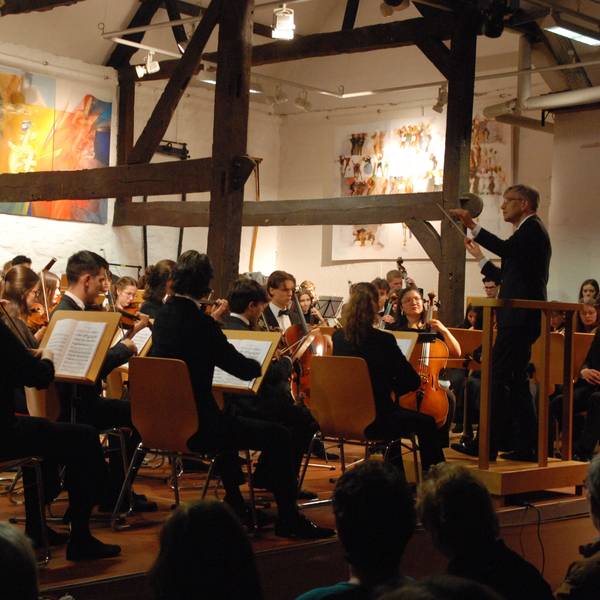 Die jungen Musiker sind schräg von hinten zu sehen, rechts steht der Dirigent.