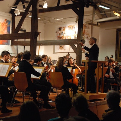 Die jungen Musiker sind schräg von hinten zu sehen, rechts steht der Dirigent.