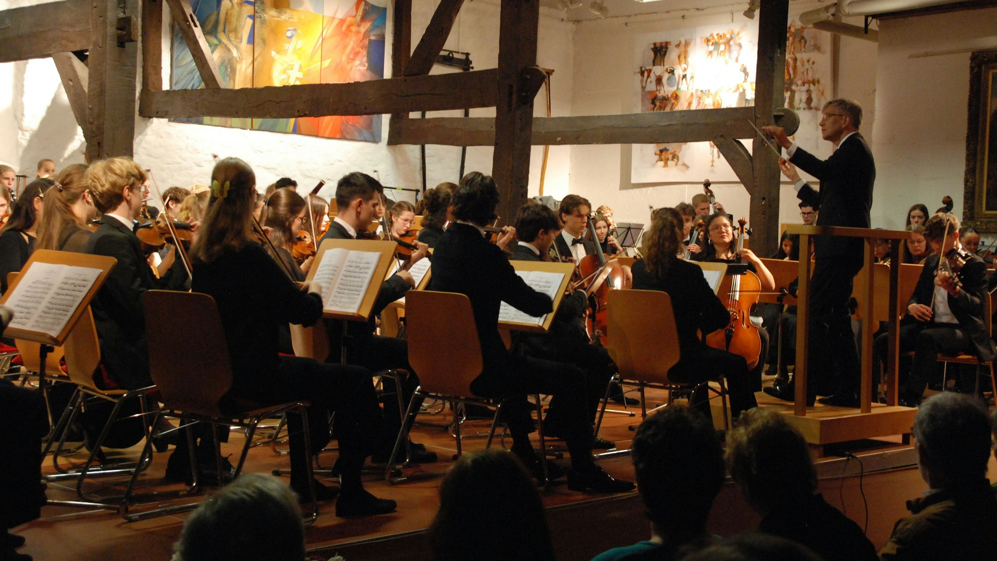 Die jungen Musiker sind schräg von hinten zu sehen, rechts steht der Dirigent.