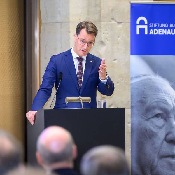 Ein Man steht an einem Pult, daneben befindet sich ein Aufsteller mit einem großen Porträt Konrad Adenauers.