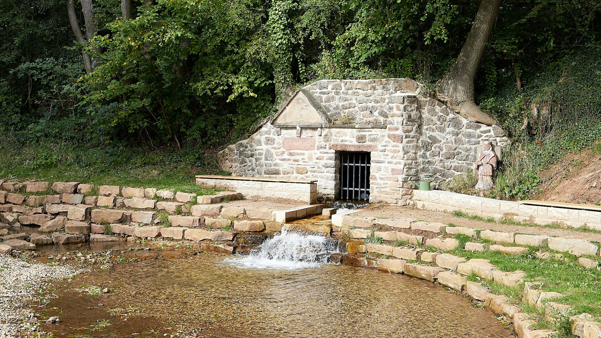 Die Erftquelle sprudelt in ein steinernes Bassin, in das man über Stufen hineinsteigen kann.