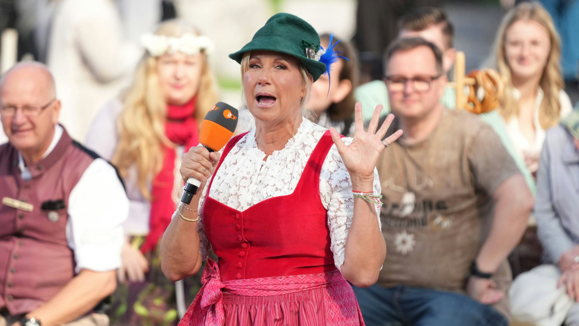 Andrea Kiewel hebt die Hand und spricht ins Mikro.