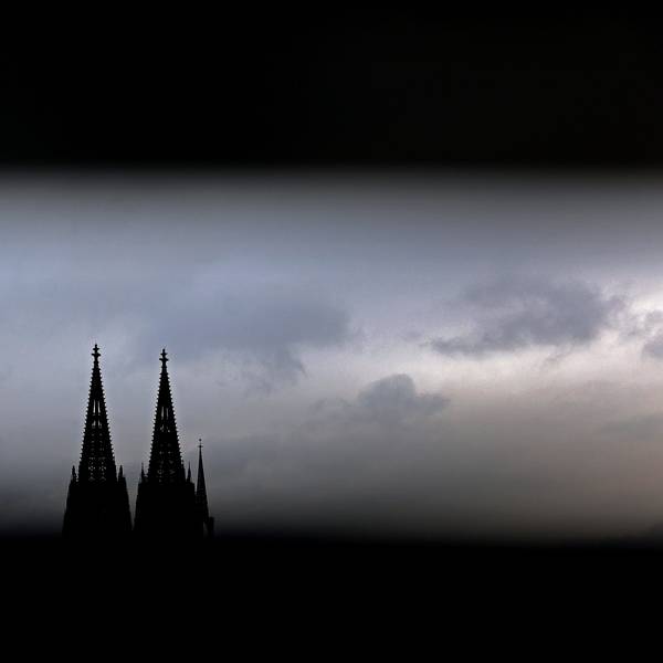 Durch ein Geländer sind die Spitzen des Kölner Doms zu sehen. Im Erzbistum Köln sind die Finanzüberschüsse 2023 eingebrochen.