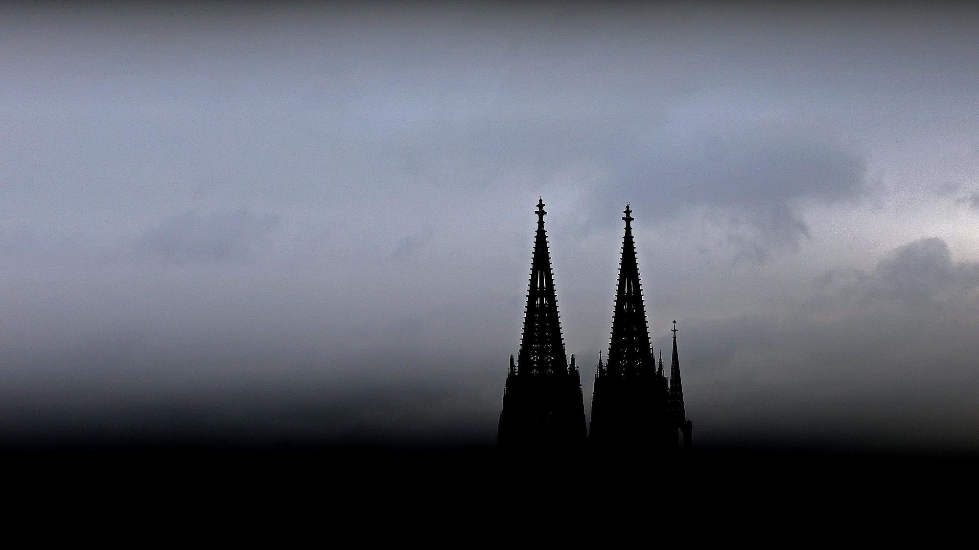 Durch ein Geländer sind die Spitzen des Kölner Doms zu sehen. Im Erzbistum Köln sind die Finanzüberschüsse 2023 eingebrochen.