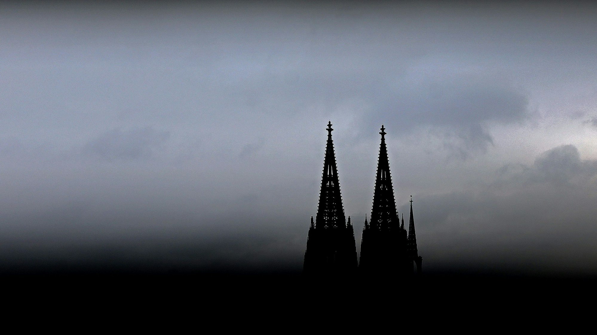 Durch ein Geländer sind die Spitzen des Kölner Doms zu sehen. Im Erzbistum Köln sind die Finanzüberschüsse 2023 eingebrochen.