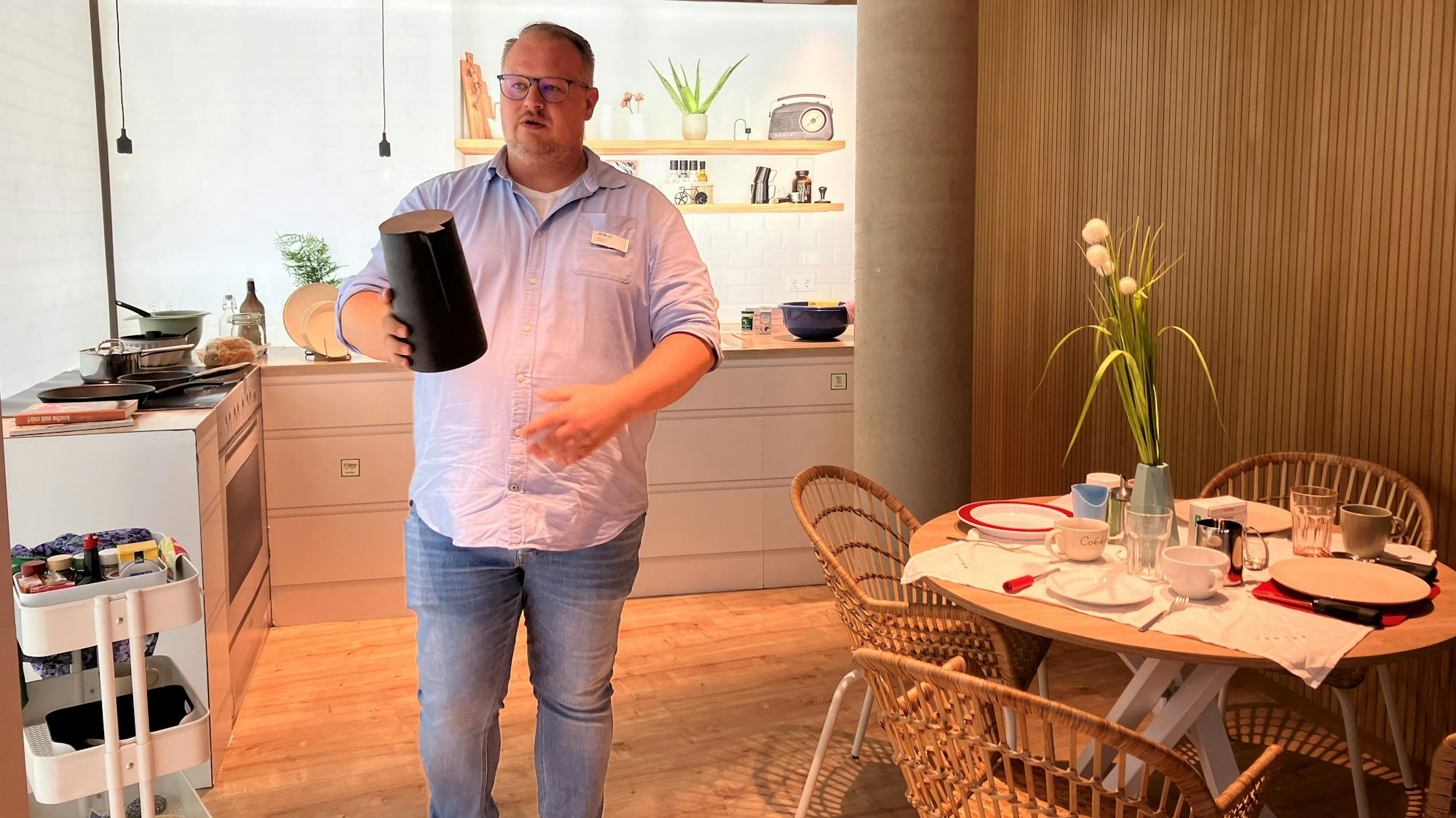 Ein Mann steht in einer Musterwohnung für Demenzkranke im AOK-Haus in Gummersbach und hält eine schwarze Kaffeekanne in der Hand.