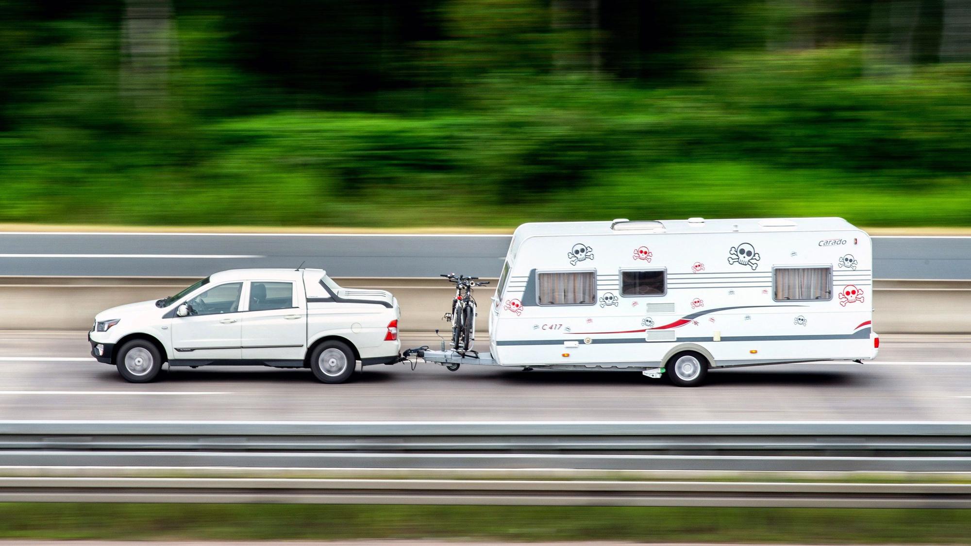 Ein Auto zieht einen Wohnwagen. Dazwischen ist auch ein Fahrrad montiert.