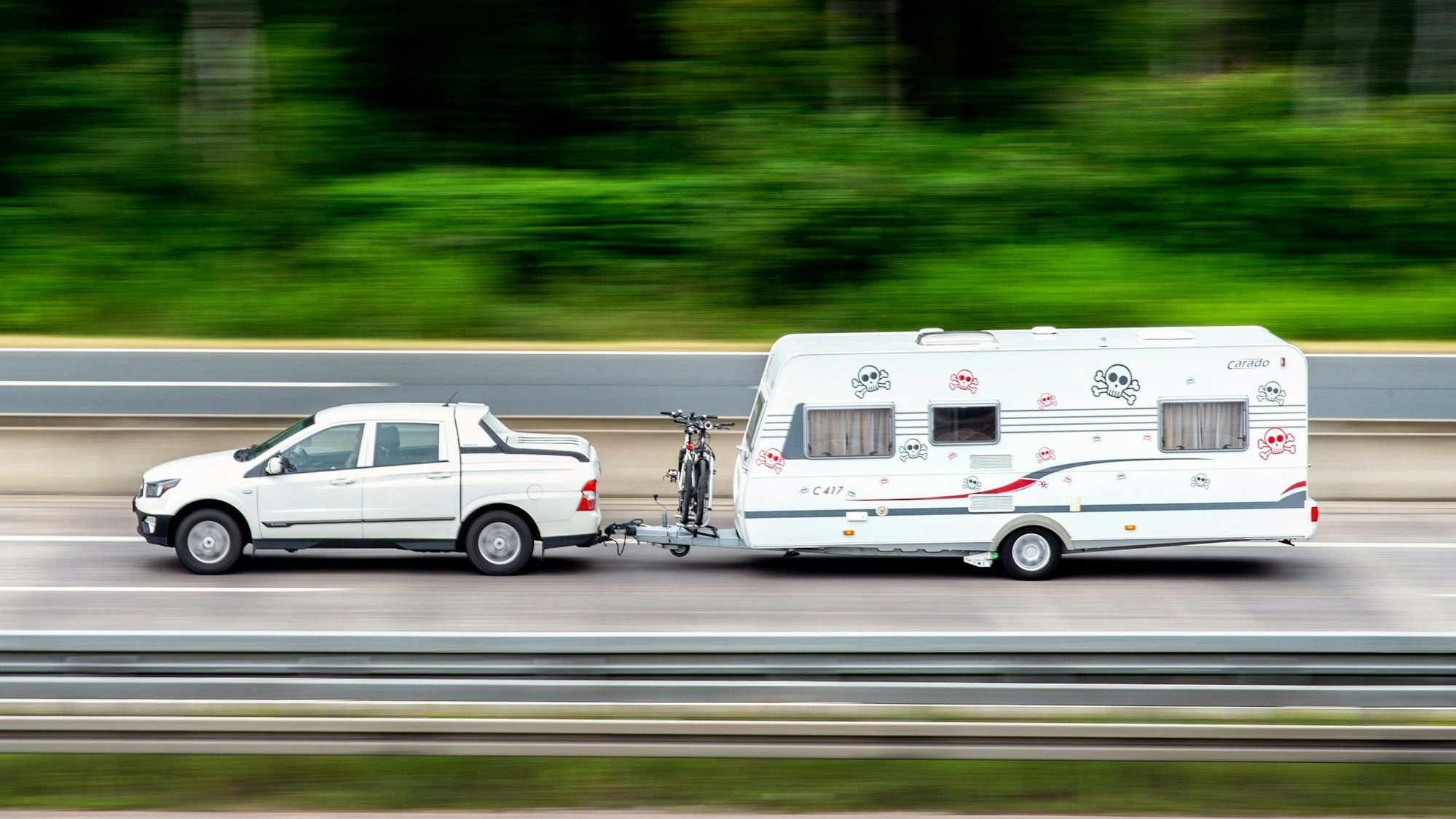Ein Auto zieht einen Wohnwagen. Dazwischen ist auch ein Fahrrad montiert.