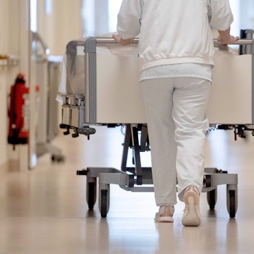 Eine Krankenpflegerin schiebt ein Krankenbett durch einen Krankenhausflur.