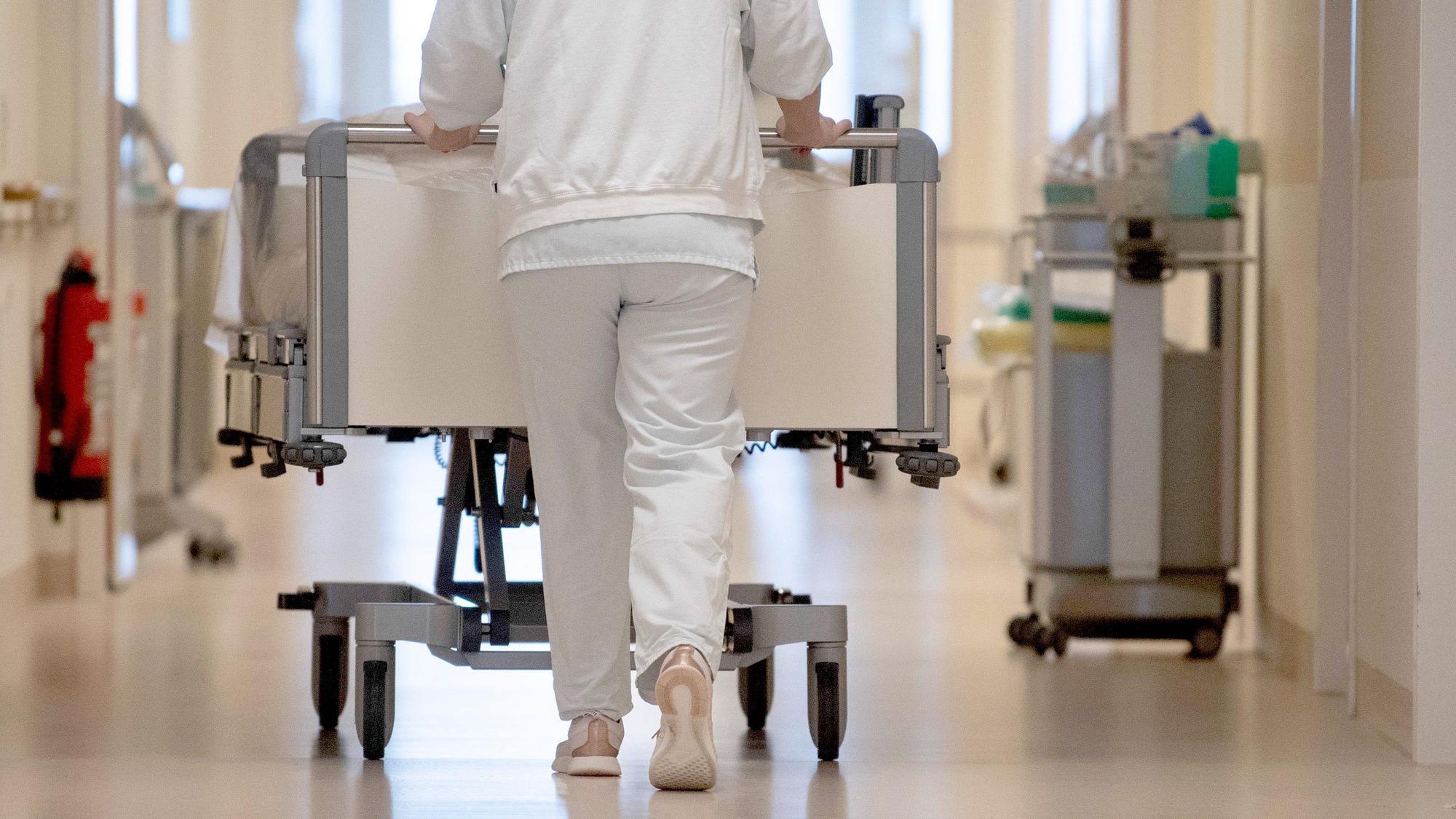 Eine Krankenpflegerin schiebt ein Krankenbett durch einen Krankenhausflur.