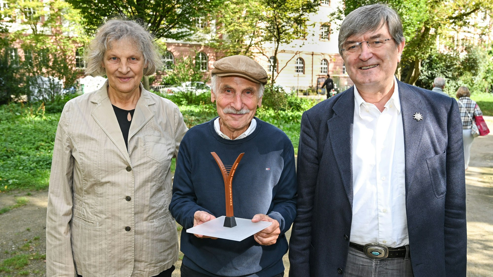 Eine Frau und zwei Männer stehen auf einem grünen Platz
