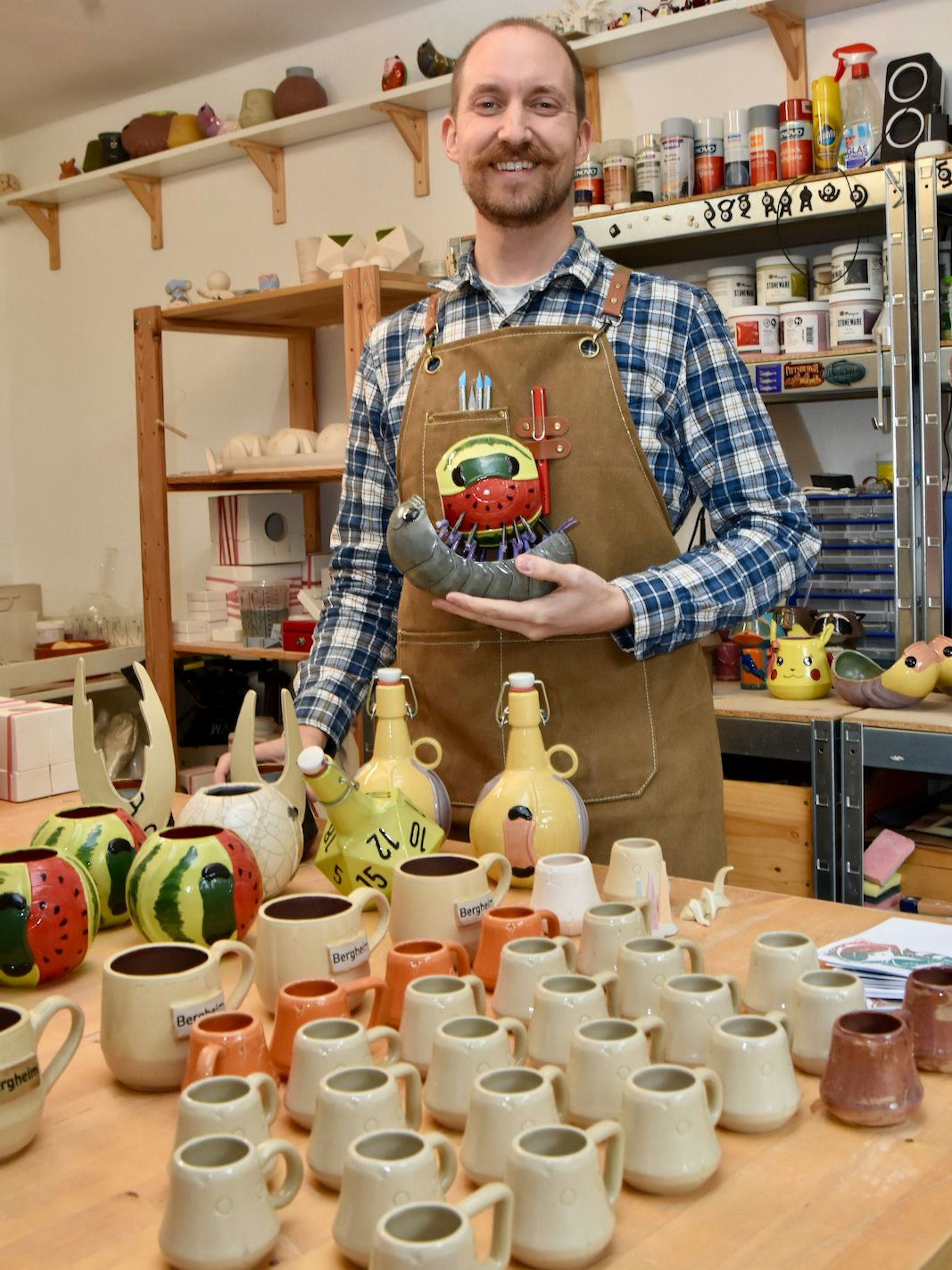 Ein lachender Mann steht vor vielen getöpferten Tassen.
