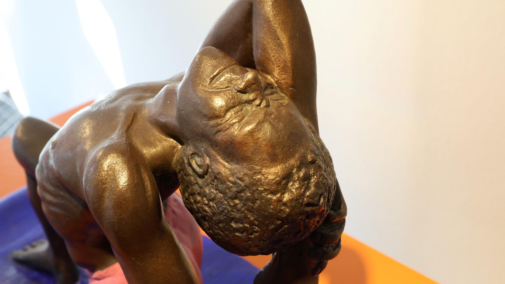 Die Bronzeskulptur stellt einen Mann dar, der auf einen blauen Matte turnt.