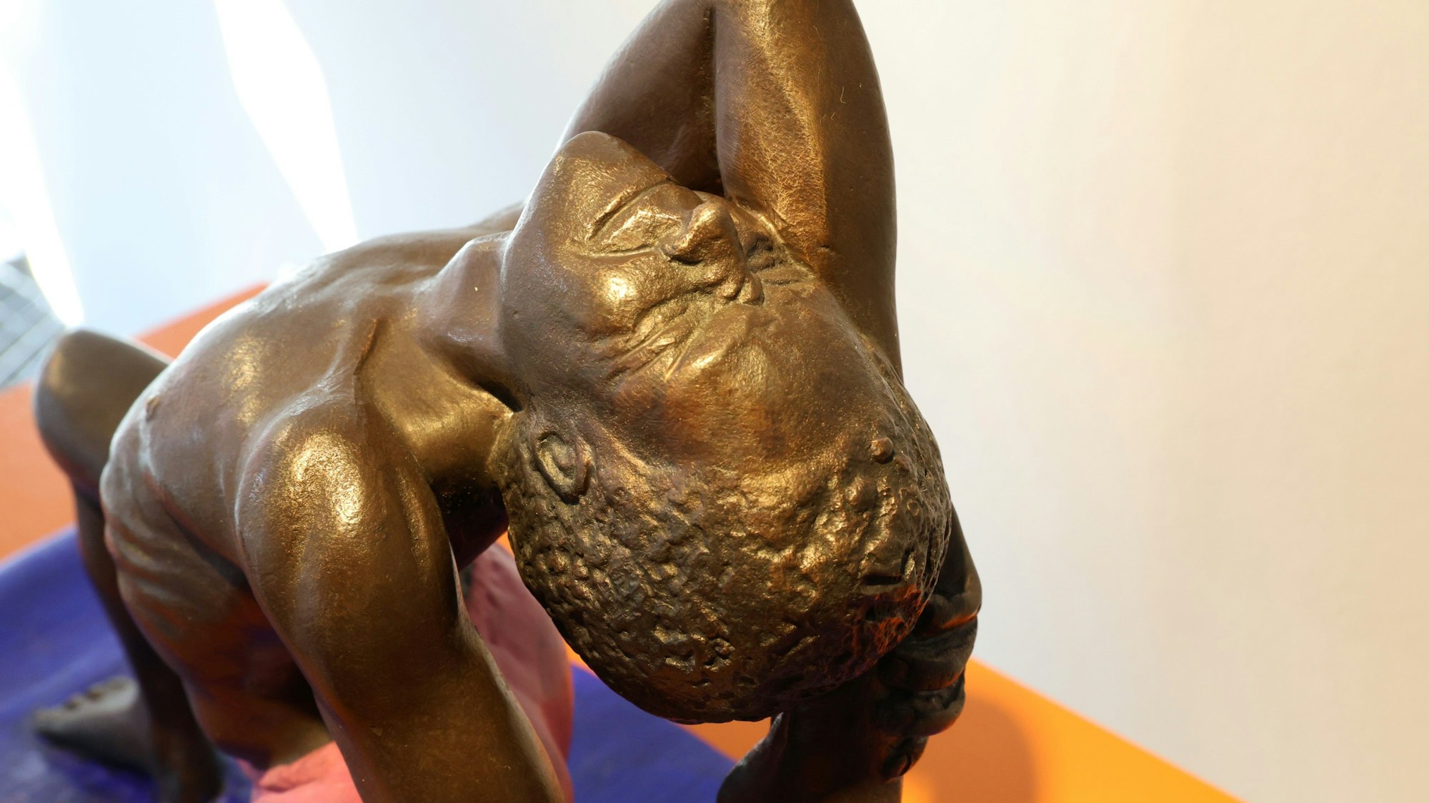 Die Bronzeskulptur stellt einen Mann dar, der auf einen blauen Matte turnt.