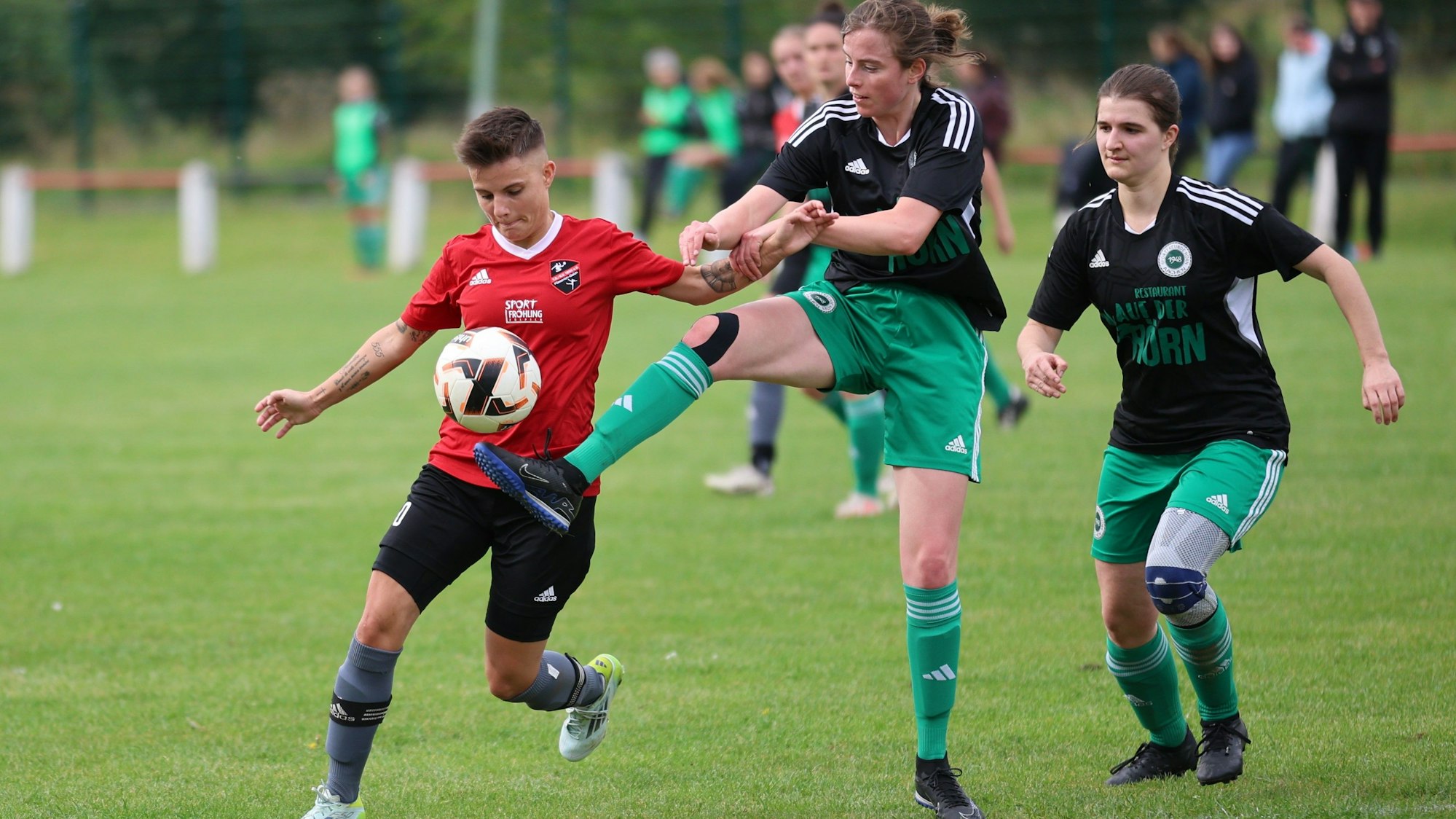 Zwei Fußballerinnen kämpfen um den Ball, eine dritte beobachtet das Duell.