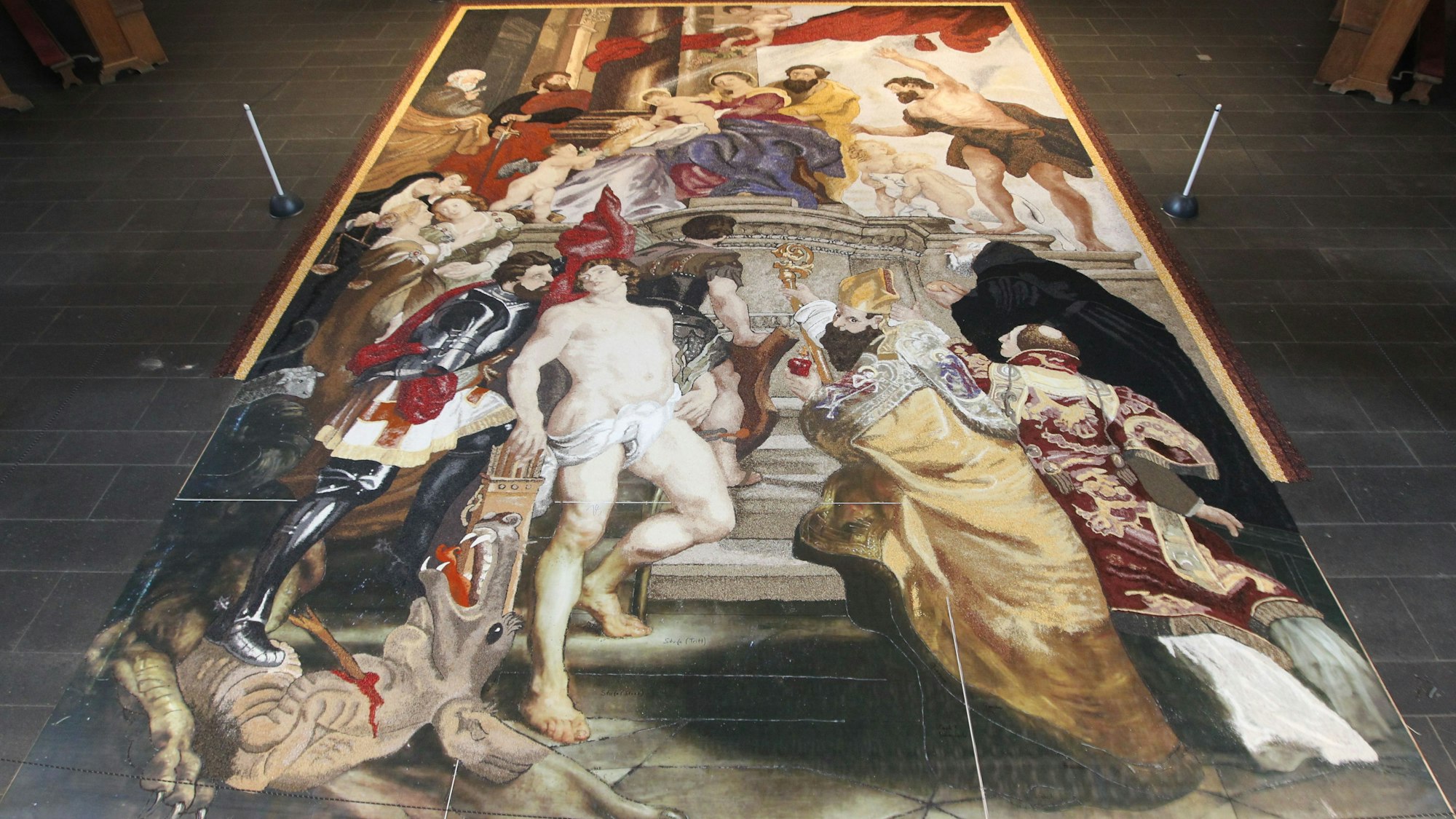 Das Bild zeigt den 30 Quadratmeter großen Erntedank-Teppich. Es ist ein Gemälde des Maler Peter Paul Rubens mit Maria, Josef, dem Jesuskind, vielen Heiligen und Putten.