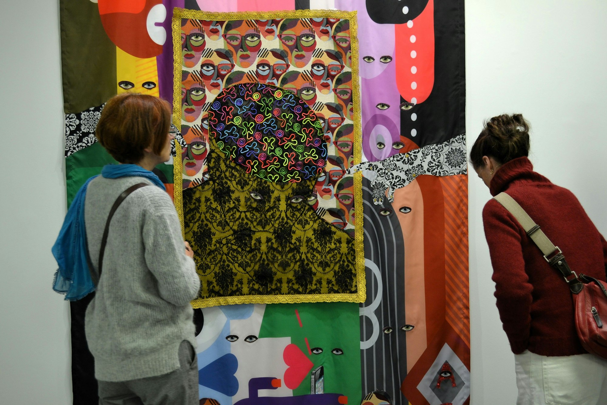 Zwei Frauen beugen sich zu einem Werk aus vielen bunten, überlappenden Tüchern mit Augen.
