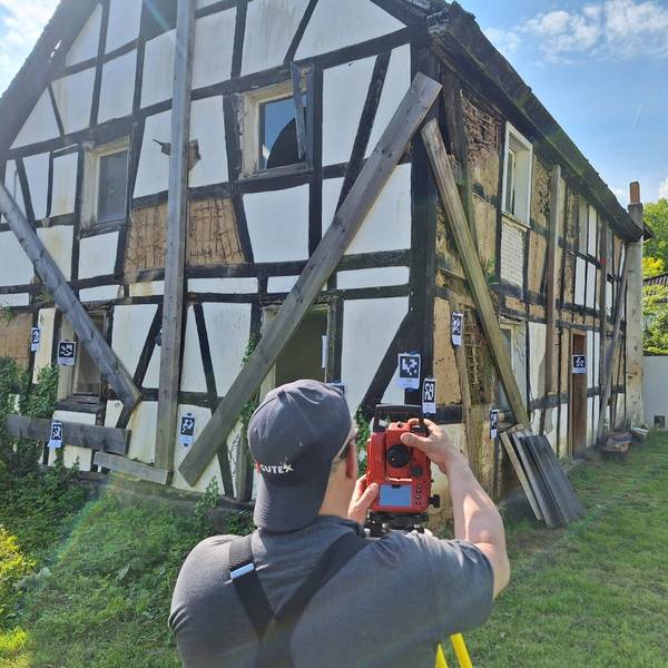Ein Mann filmt ein baufälliges Fachwerkhaus, an dem Markierungen angebracht sind.