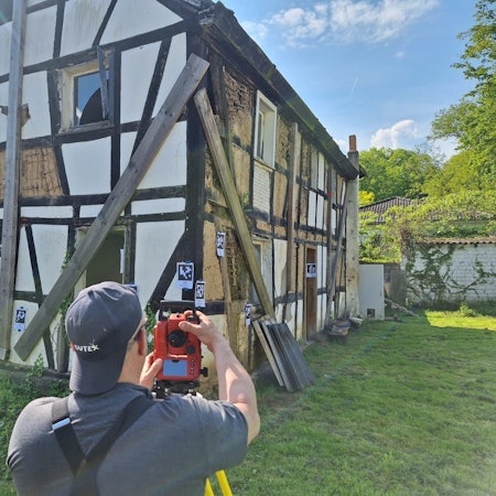Ein Mann filmt ein baufälliges Fachwerkhaus, an dem Markierungen angebracht sind.