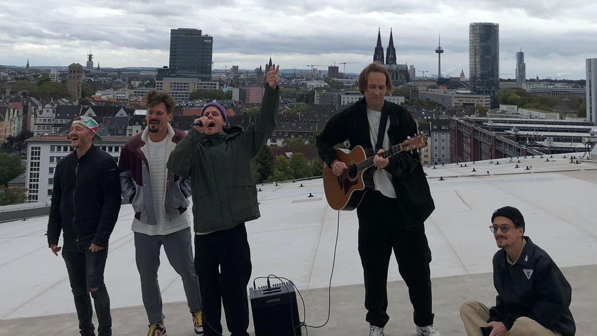 Die Bandmitglieder singen auf dem Dach der Lanxess-Arena.