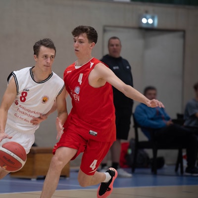 Ein Basketballer des TuS Zülpich im weißen Trikot dribbelt den Ball an seinem Kontrahenten von den Erftbaskets vorbei.