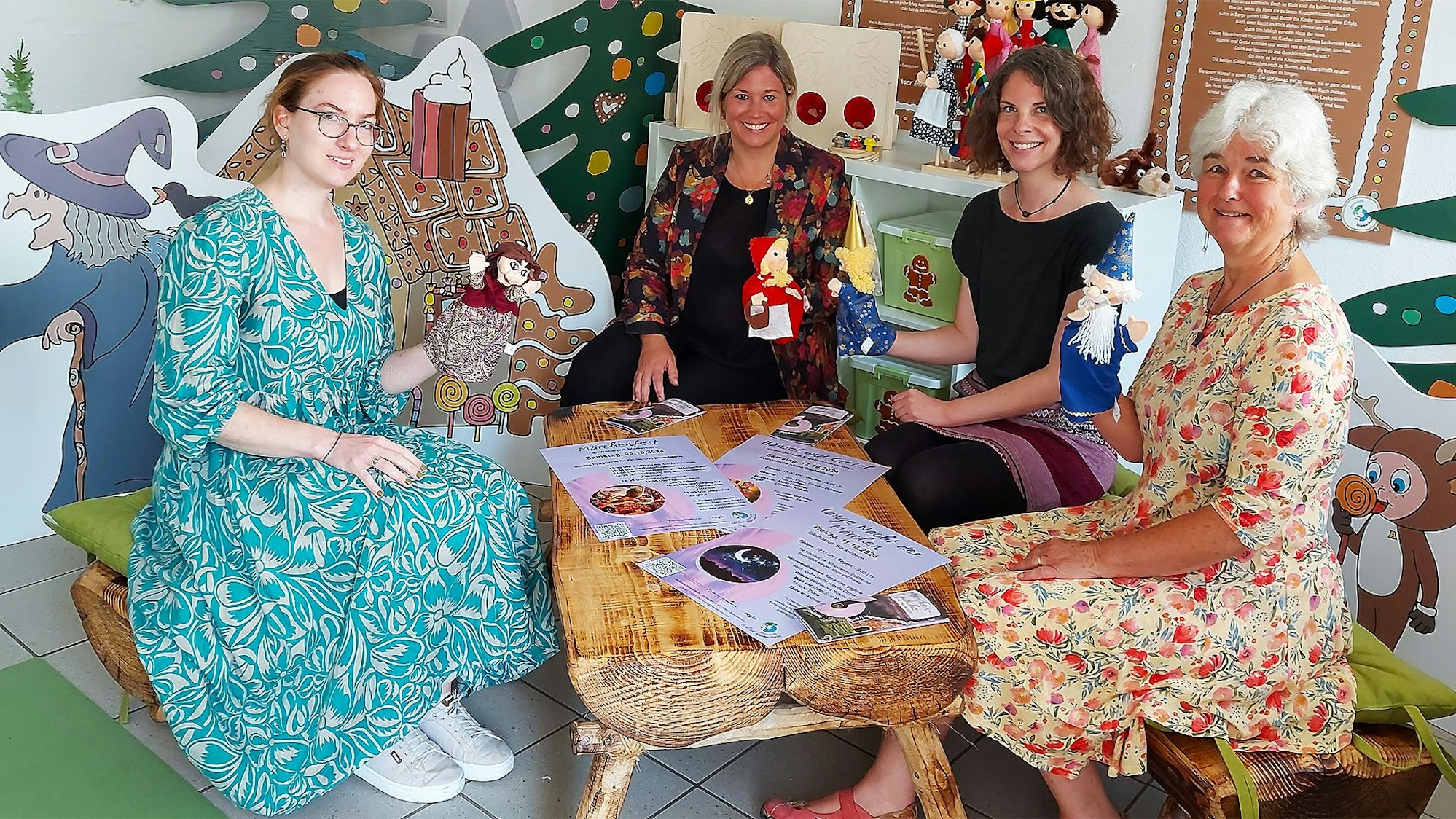 Vier Frauen sitzen an einem Holztisch. Das Zimmer ist mit Aufstellern mit Märchenfiguren dekoriert.
