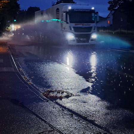 Ein Lkw fährt durch eine große Pfütze und Wasser spritzt hoch.