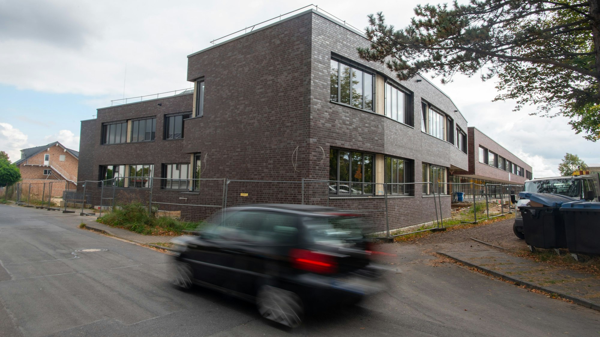 Ein Auto fährt an dem fast fertigen Erweiterungsbau am Schulcampus Zülpich vorbei. Das Gebäude steht hinter einem Bauzaun, rechts im Bild sind Mülltonnen zu erkennen.