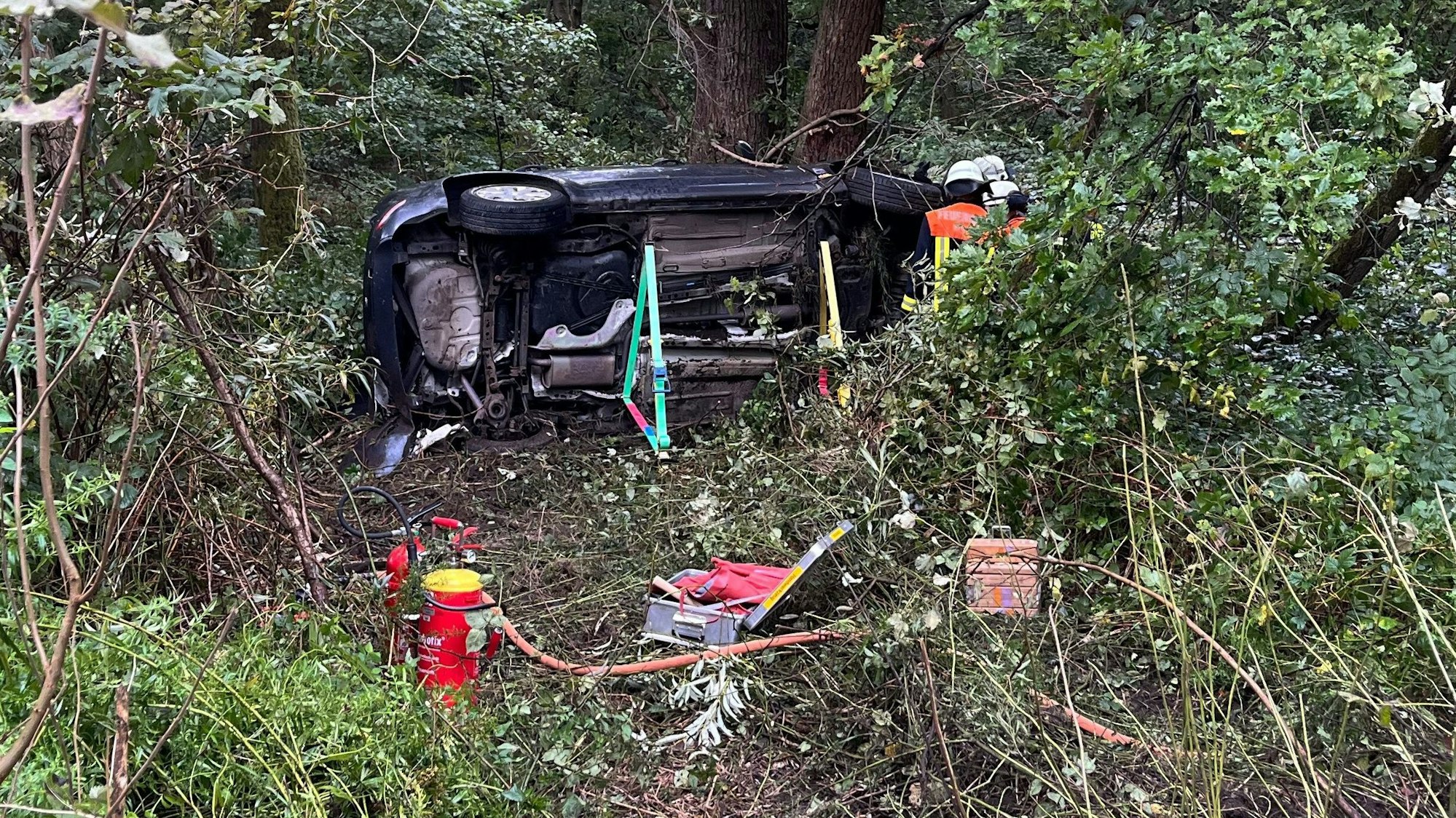Ein Pkw überschlug sich mehrfach und blieb auf der Seite liegen. Feuerwehrleute sichern das Fahrzeug.