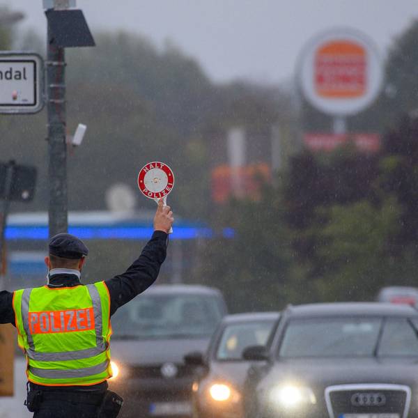 Ein Polizist winkt mit einer Polizeikelle einen Autofahrer aus dem Straßenverkehr.