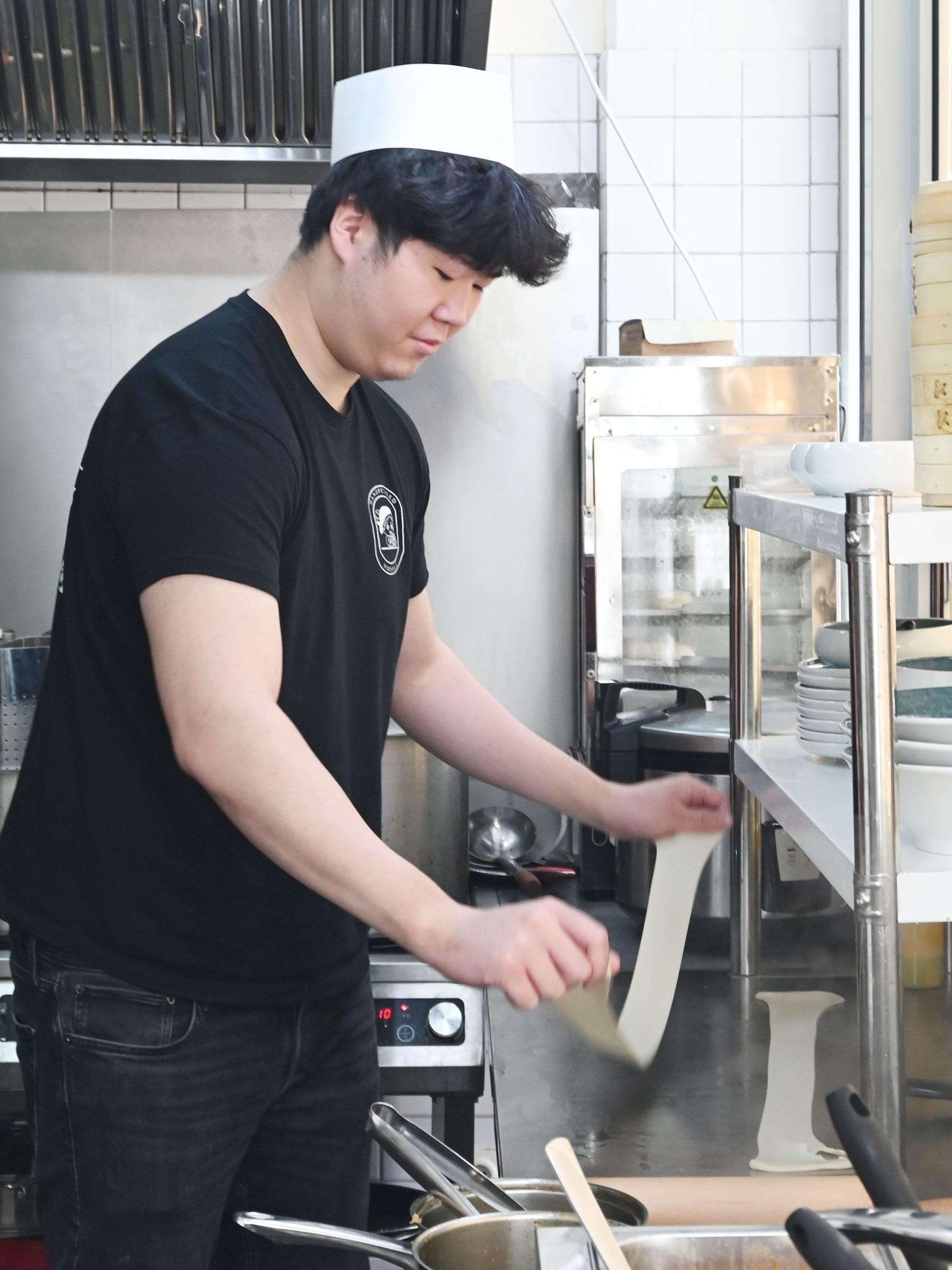 Für die Nudelzubereitung zieht ein Mann Teig in der Restaurantküche auseinander.