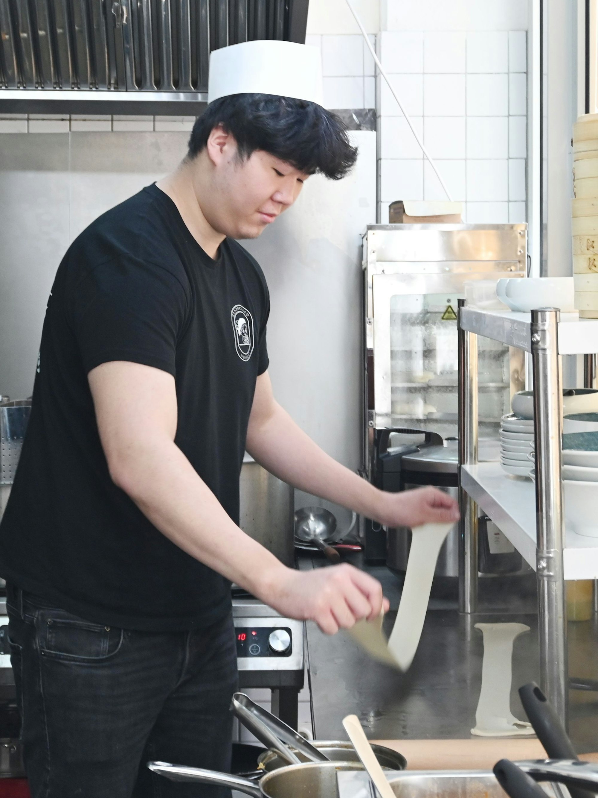 Für die Nudelzubereitung zieht ein Mann Teig in der Restaurantküche auseinander.