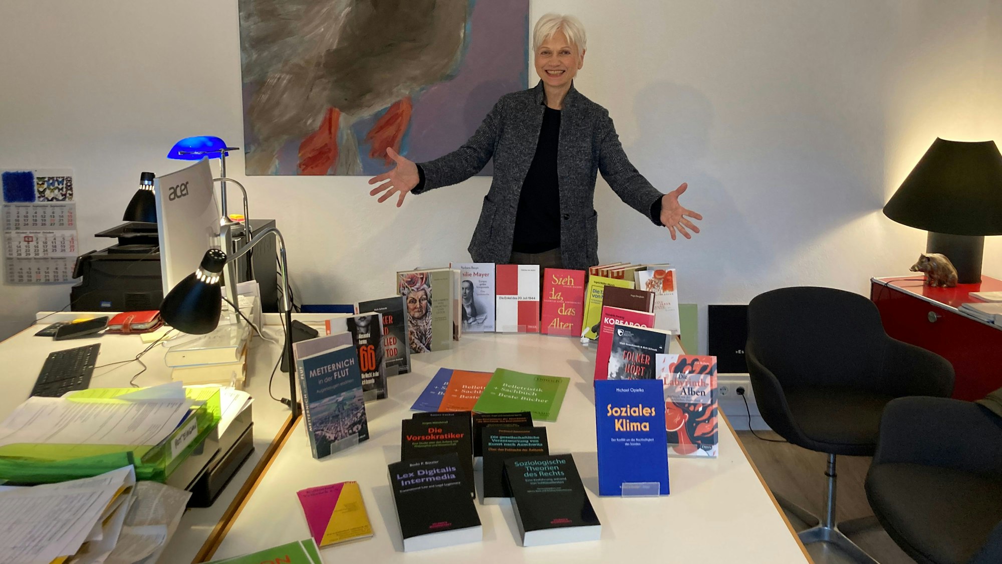 Eine Frau steht mit weit geöffneten Armen vor einem Tisch, auf dem Bücher stehen.