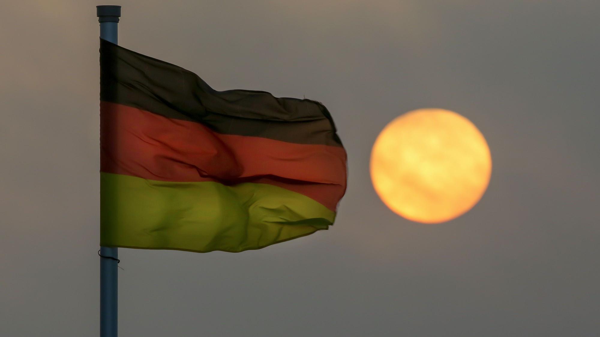 Hinter einer Flagge der Bundesrepublik Deutschland geht am Morgen im Nebel die Sonne auf. (Symbolbild)