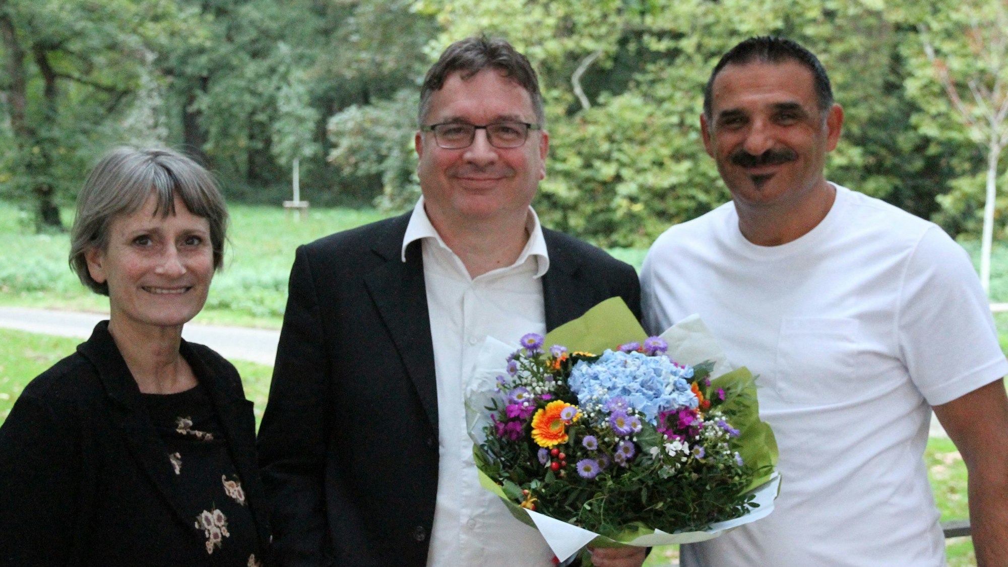 Eine Frau und zwei Männer, einer davon mit Blumenstrauß