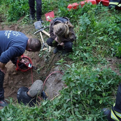 Ein Mann steht in einem Dachsbau. Ein weiterer Mann und eine Frau beugen sich vor und schauen auf ein Display einer Spezialkamera.