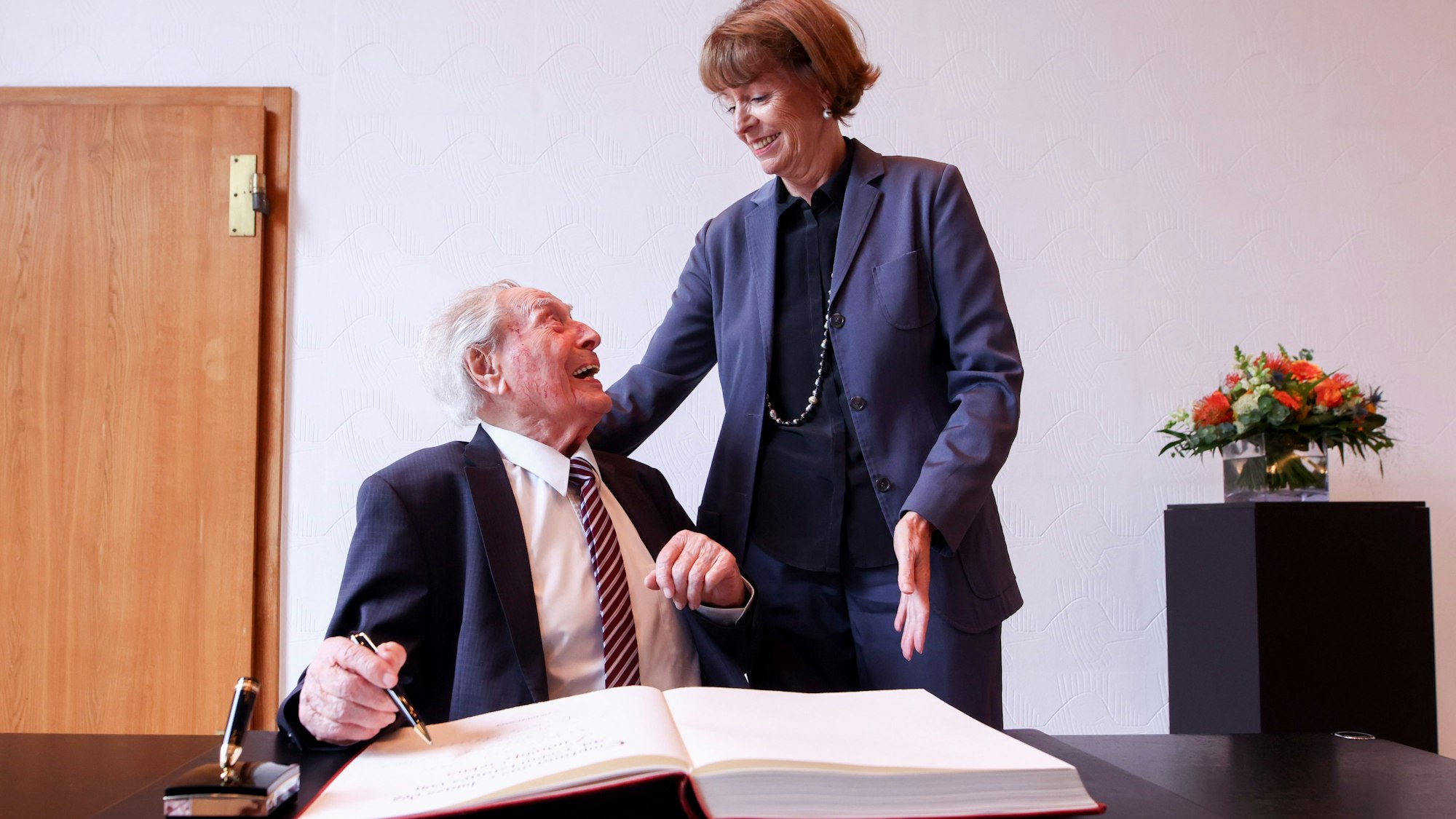 Ludwig Sebus trägt sich ins Gästebuch der Stadt Köln ein, neben ihm steht Henriette Reker.