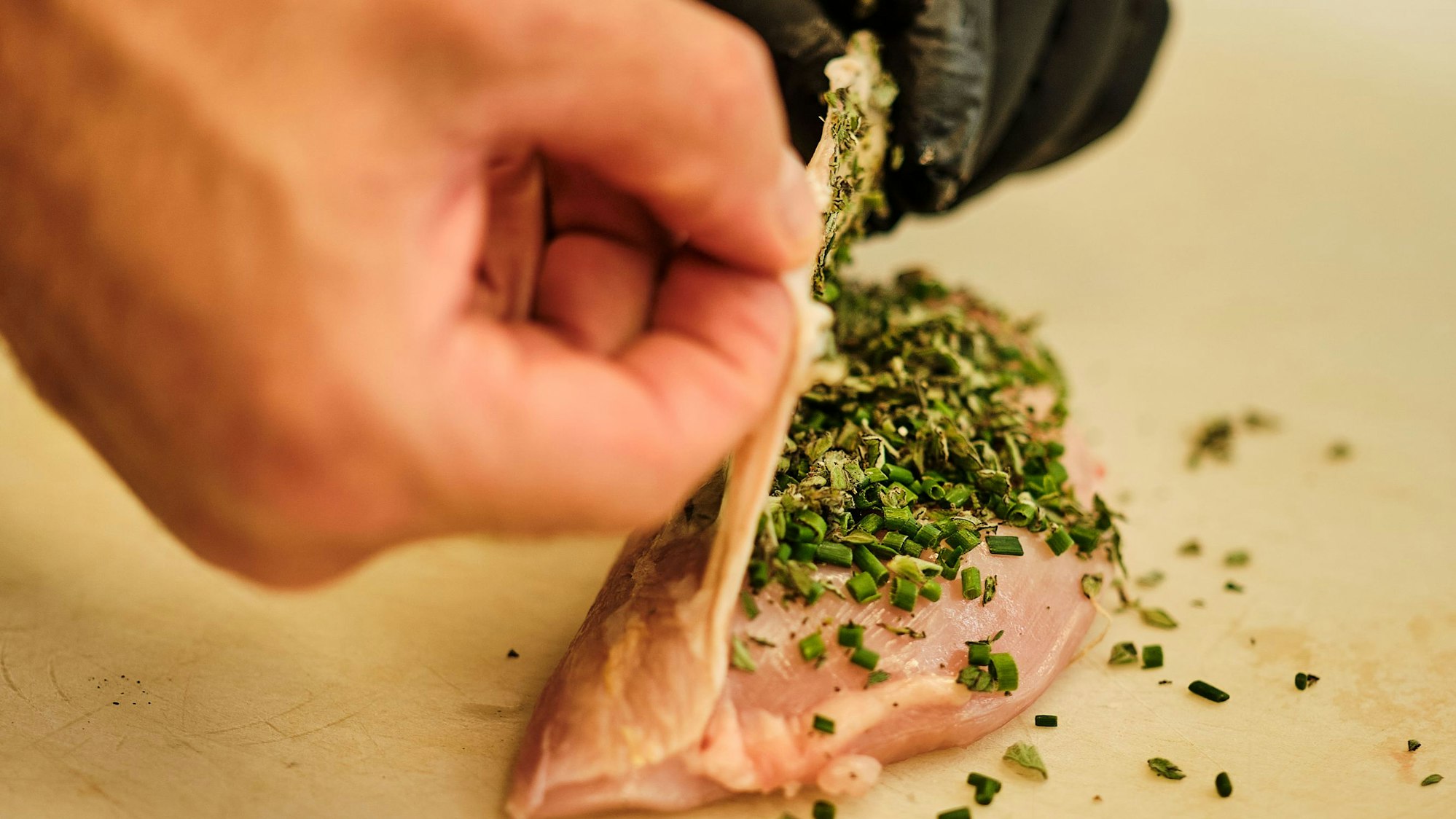 Die Haut der Poularden-Brust mit den Fingern an der Seite leicht lösen und die Kräuter darunter verteilen.