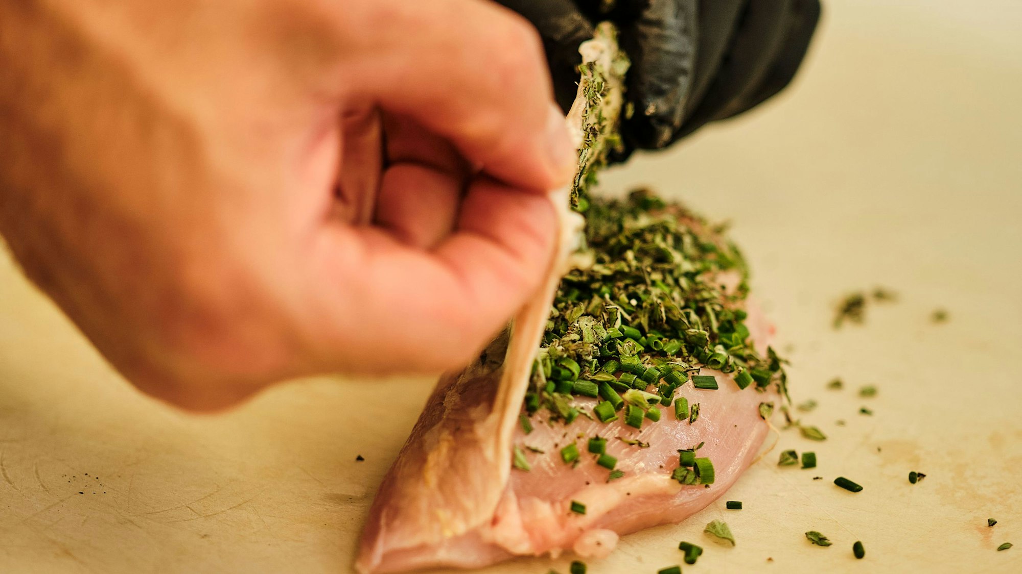 Die Haut der Poularden-Brust mit den Fingern an der Seite leicht lösen und die Kräuter darunter verteilen.