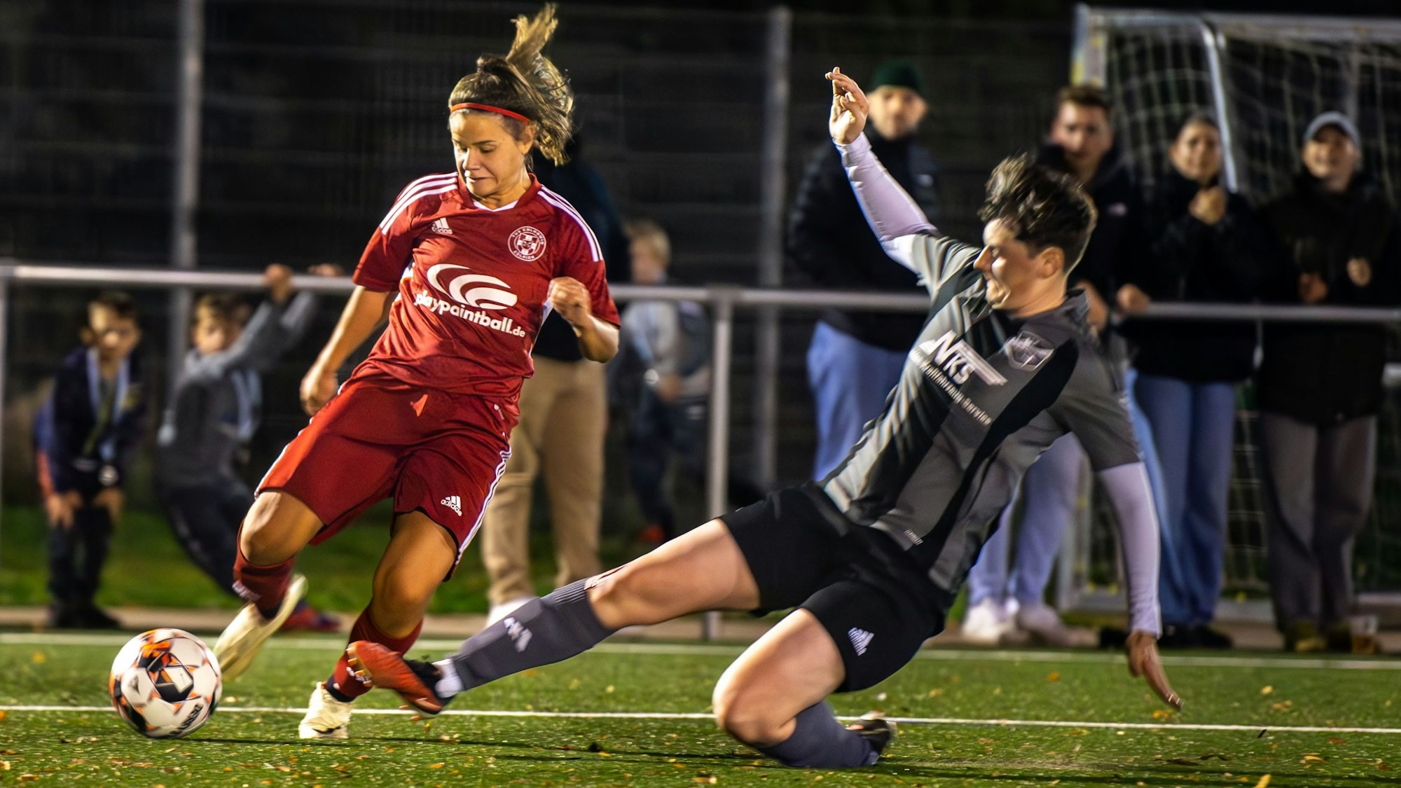Carlotta Aldenkirch im roten Trikot des TuS Zülpich spielt den Ball, Jana Stark kann auch mit einer Grätsche die Flanke nicht verhindern.